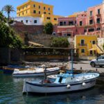Scorcio del Porto Romano di Ventotene con barche da pesca ormeggiate e palazzi storici colorati sullo sfondo sotto un cielo azzurro.