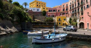 Scorcio del Porto Romano di Ventotene con barche da pesca ormeggiate e palazzi storici colorati sullo sfondo sotto un cielo azzurro.