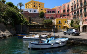 Scorcio del Porto Romano di Ventotene con barche da pesca ormeggiate e palazzi storici colorati sullo sfondo sotto un cielo azzurro.