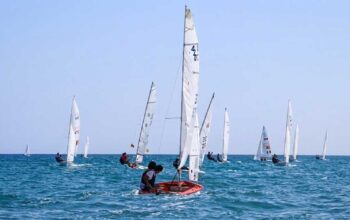 Flotta di imbarcazioni a vela e derive in gara sul mare davanti alla costa durante la Prosecco's Cup