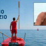 Bagnino su pattino di salvataggio alza un remo verso il cielo in segno di rispetto, con un ritratto di Fabrizio Valente e la scritta "BUON VIAGGIO FABRIZIO".