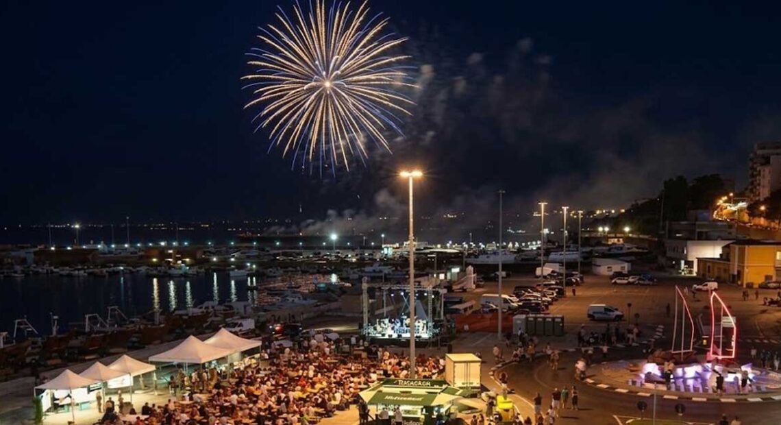 Veduta aerea notturna del piazzale del porto di Termoli affollato per la Sagra del Pesce con spettacolo di fuochi d'artificio