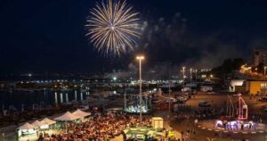 Veduta aerea notturna del piazzale del porto di Termoli affollato per la Sagra del Pesce con spettacolo di fuochi d'artificio