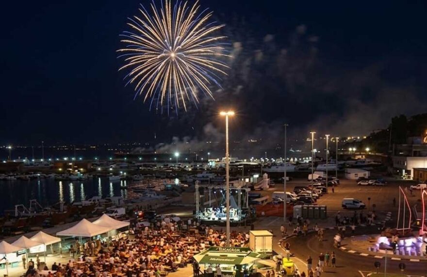 Veduta aerea notturna del piazzale del porto di Termoli affollato per la Sagra del Pesce con spettacolo di fuochi d'artificio