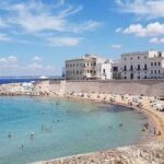 Veduta dall'alto della Spiaggia della Purità a Gallipoli con i bagnanti e il centro storico fortificato sullo sfondo