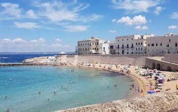 Veduta dall'alto della Spiaggia della Purità a Gallipoli con i bagnanti e il centro storico fortificato sullo sfondo