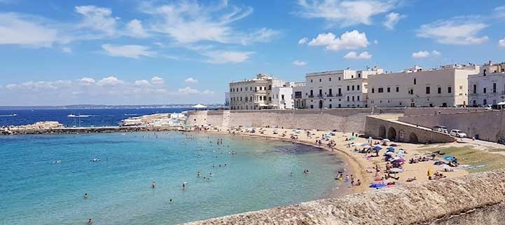 Veduta dall'alto della Spiaggia della Purità a Gallipoli con i bagnanti e il centro storico fortificato sullo sfondo