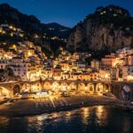 Vista panoramica notturna del borgo e della spiaggia di Atrani illuminata in Costiera Amalfitana.