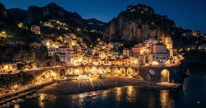 Vista panoramica notturna del borgo e della spiaggia di Atrani illuminata in Costiera Amalfitana.