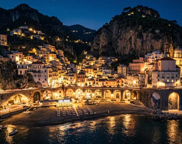 Vista panoramica notturna del borgo e della spiaggia di Atrani illuminata in Costiera Amalfitana.