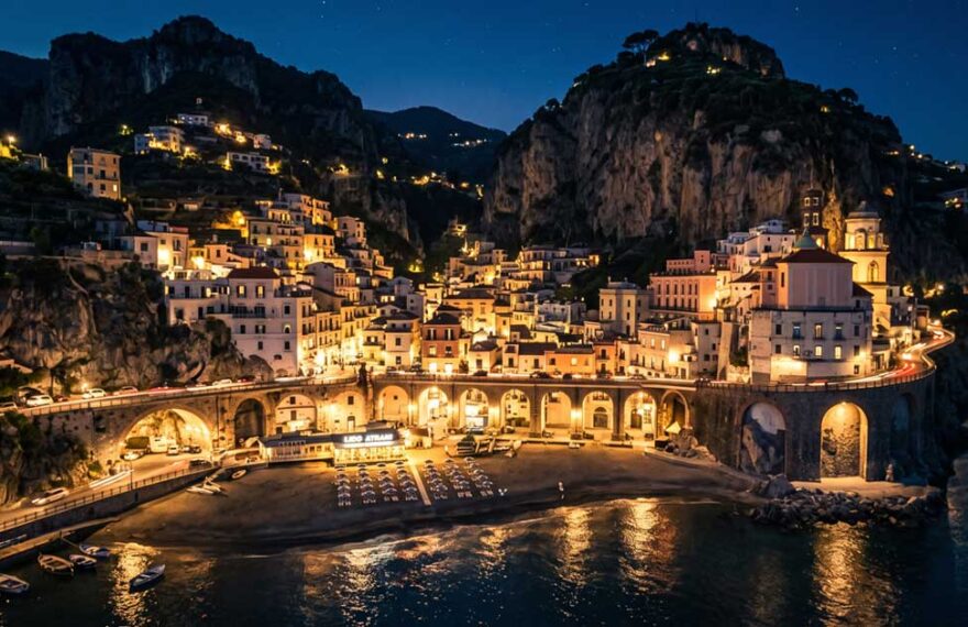 Vista panoramica notturna del borgo e della spiaggia di Atrani illuminata in Costiera Amalfitana.