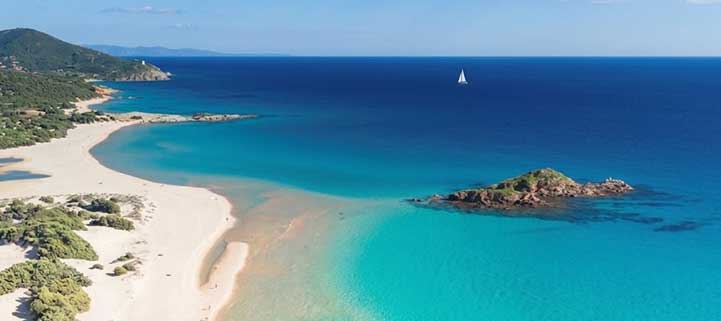 La spiaggia di Su Giudeu a Chia con la sabbia bianca, il mare cristallino e l'omonimo isolotto sullo sfondo.