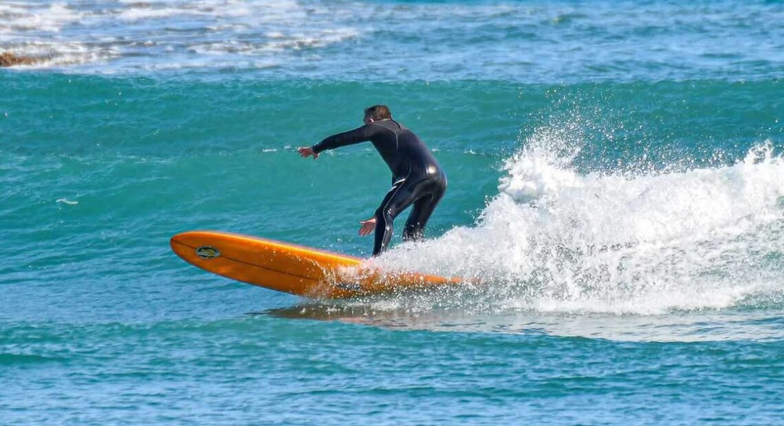 Un surfista in muta nera in equilibrio su una tavola arancione tra le onde del mare ligure.