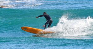 Un surfista in muta nera in equilibrio su una tavola arancione tra le onde del mare ligure.