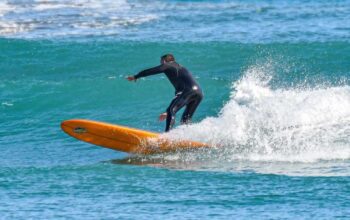 Un surfista in muta nera in equilibrio su una tavola arancione tra le onde del mare ligure.
