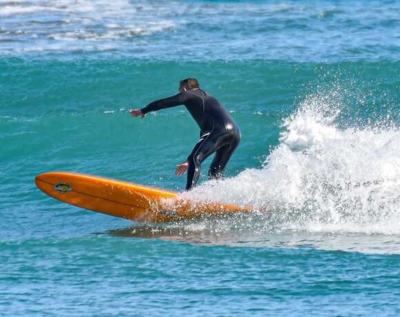 Un surfista in muta nera in equilibrio su una tavola arancione tra le onde del mare ligure.