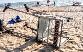 Torretta di salvataggio rovesciata sulla sabbia dopo un atto vandalico in spiaggia.