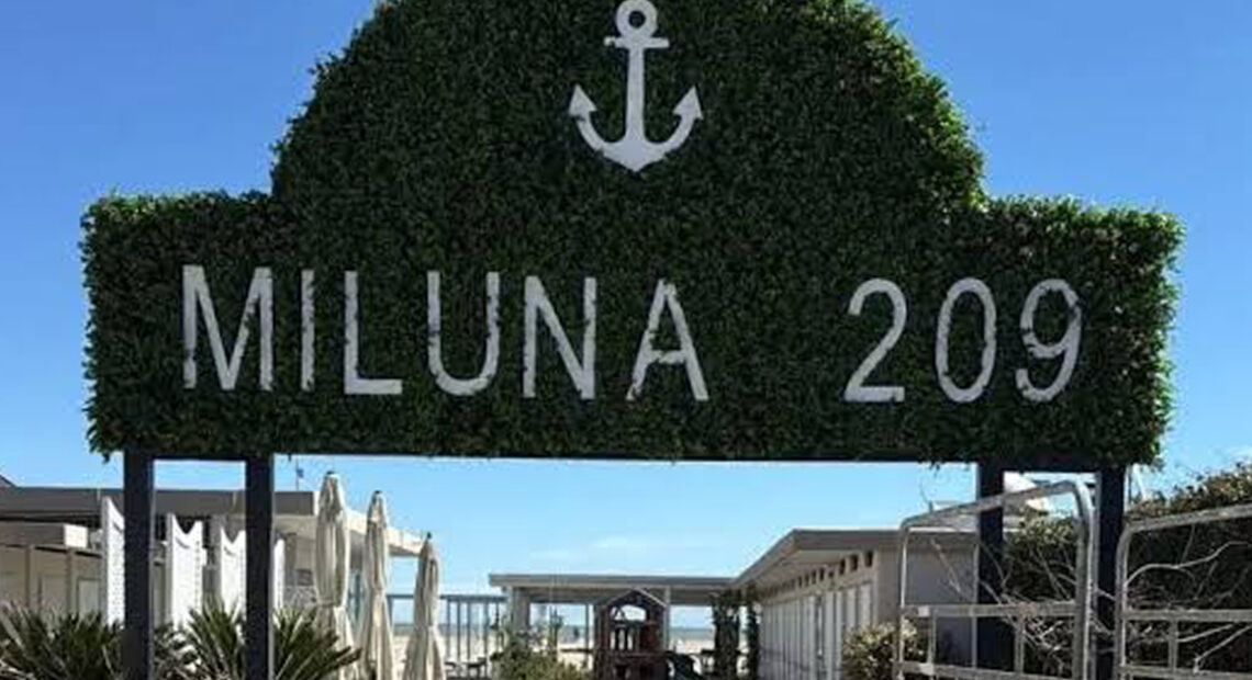 Insegna in verde dello stabilimento balneare Miluna 209 a Cervia con l'ancora e il camminamento d'ingresso.