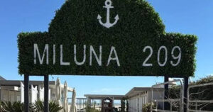 Insegna in verde dello stabilimento balneare Miluna 209 a Cervia con l'ancora e il camminamento d'ingresso.