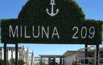 Insegna in verde dello stabilimento balneare Miluna 209 a Cervia con l'ancora e il camminamento d'ingresso.