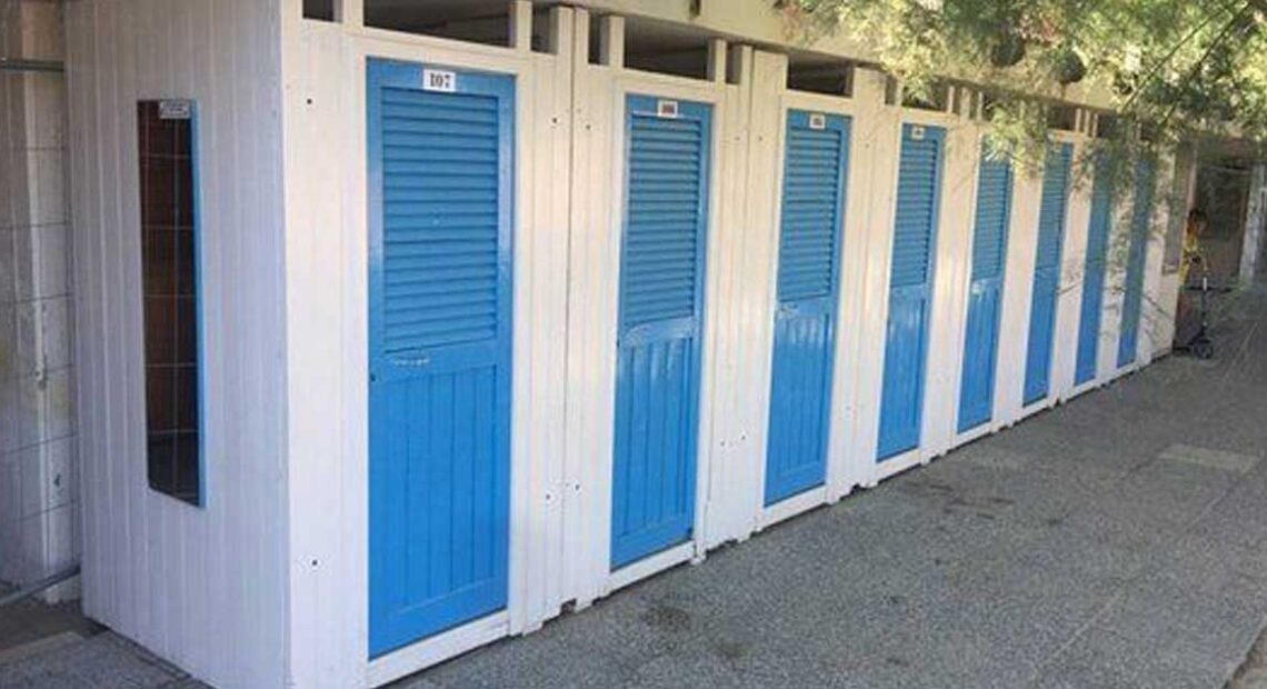 Fila di cabine balneari in legno bianche con porte blu allo stabilimento Bagni Colombo di Spotorno