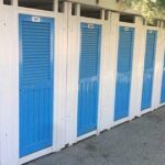 Fila di cabine balneari in legno bianche con porte blu allo stabilimento Bagni Colombo di Spotorno