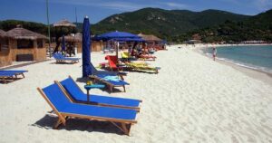 Spiaggia dell'Isola d'Elba con sabbia bianca, lettini blu e ombrelloni con colline sullo sfondo