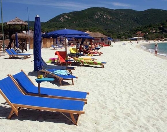 Spiaggia dell'Isola d'Elba con sabbia bianca, lettini blu e ombrelloni con colline sullo sfondo
