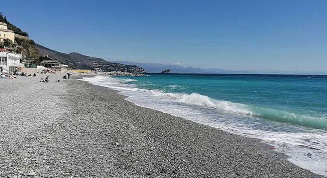 Spiaggia di ciottoli sulla costa ligure a Genova con mare limpido e strutture balneari sullo sfondo.