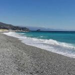 Spiaggia di ciottoli sulla costa ligure a Genova con mare limpido e strutture balneari sullo sfondo.