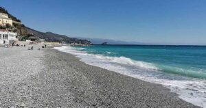 Spiaggia di ciottoli sulla costa ligure a Genova con mare limpido e strutture balneari sullo sfondo.