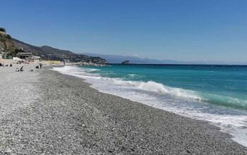 Spiaggia di ciottoli sulla costa ligure a Genova con mare limpido e strutture balneari sullo sfondo.