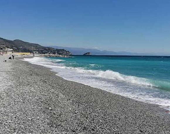Spiaggia di ciottoli sulla costa ligure a Genova con mare limpido e strutture balneari sullo sfondo.