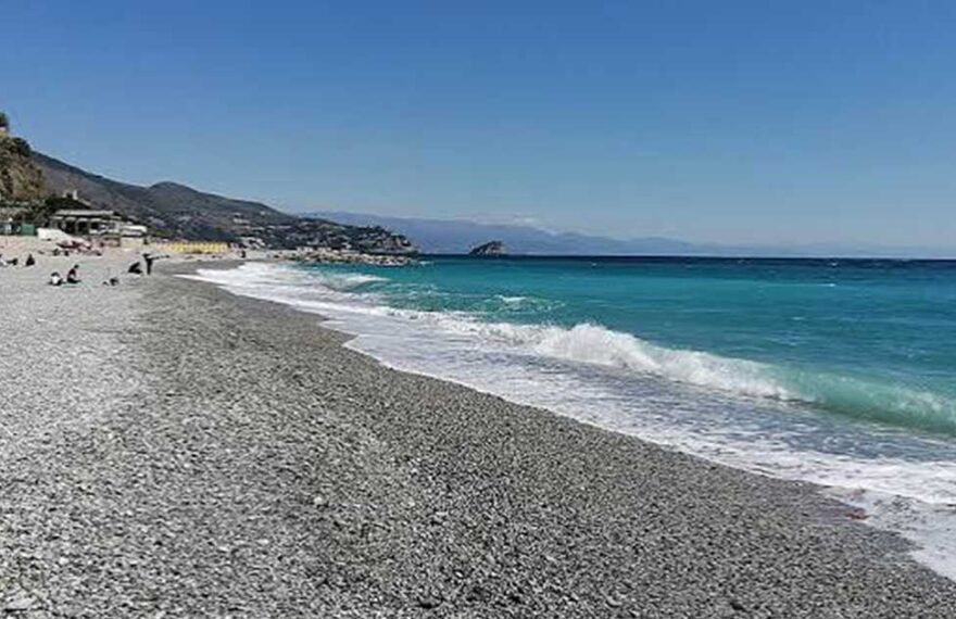 Spiaggia di ciottoli sulla costa ligure a Genova con mare limpido e strutture balneari sullo sfondo.