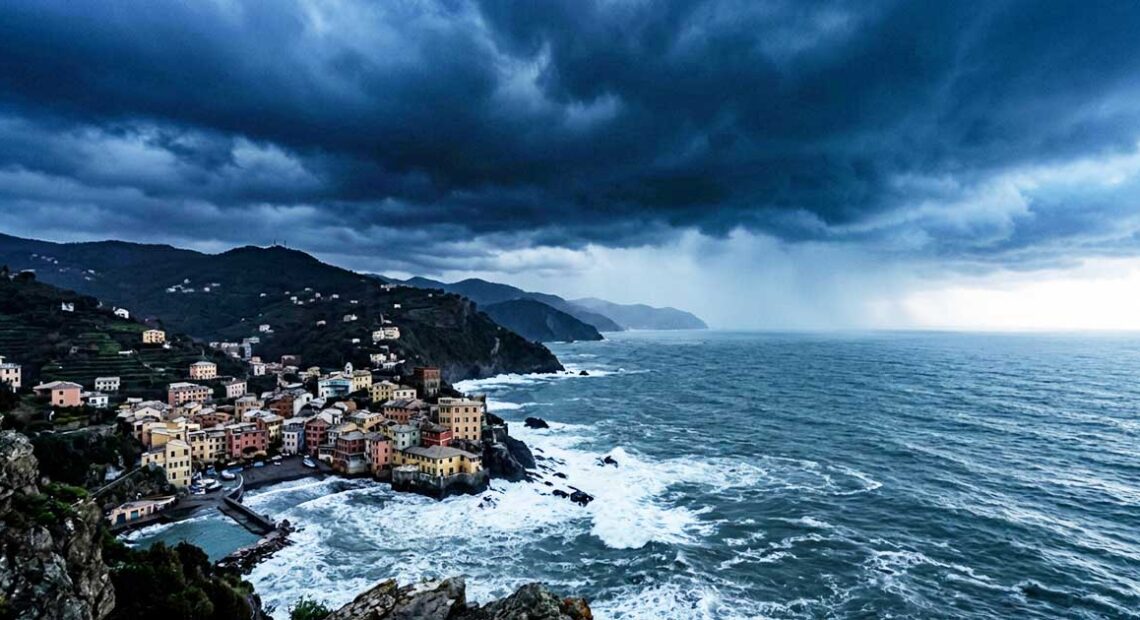 Veduta panoramica e cupa della costa ligure rocciosa con un borgo marinaro sotto un cielo nero, tempestoso e minaccioso, che evoca ansia e preoccupazione.