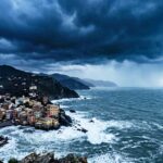 Veduta panoramica e cupa della costa ligure rocciosa con un borgo marinaro sotto un cielo nero, tempestoso e minaccioso, che evoca ansia e preoccupazione.