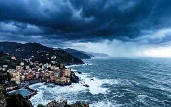 Veduta panoramica e cupa della costa ligure rocciosa con un borgo marinaro sotto un cielo nero, tempestoso e minaccioso, che evoca ansia e preoccupazione.