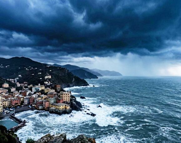 Veduta panoramica e cupa della costa ligure rocciosa con un borgo marinaro sotto un cielo nero, tempestoso e minaccioso, che evoca ansia e preoccupazione.