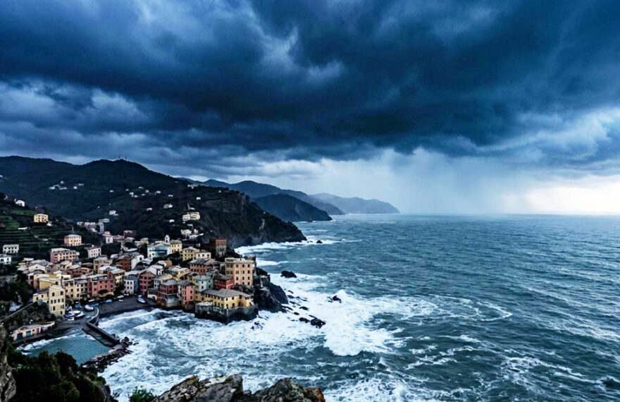 Veduta panoramica e cupa della costa ligure rocciosa con un borgo marinaro sotto un cielo nero, tempestoso e minaccioso, che evoca ansia e preoccupazione.