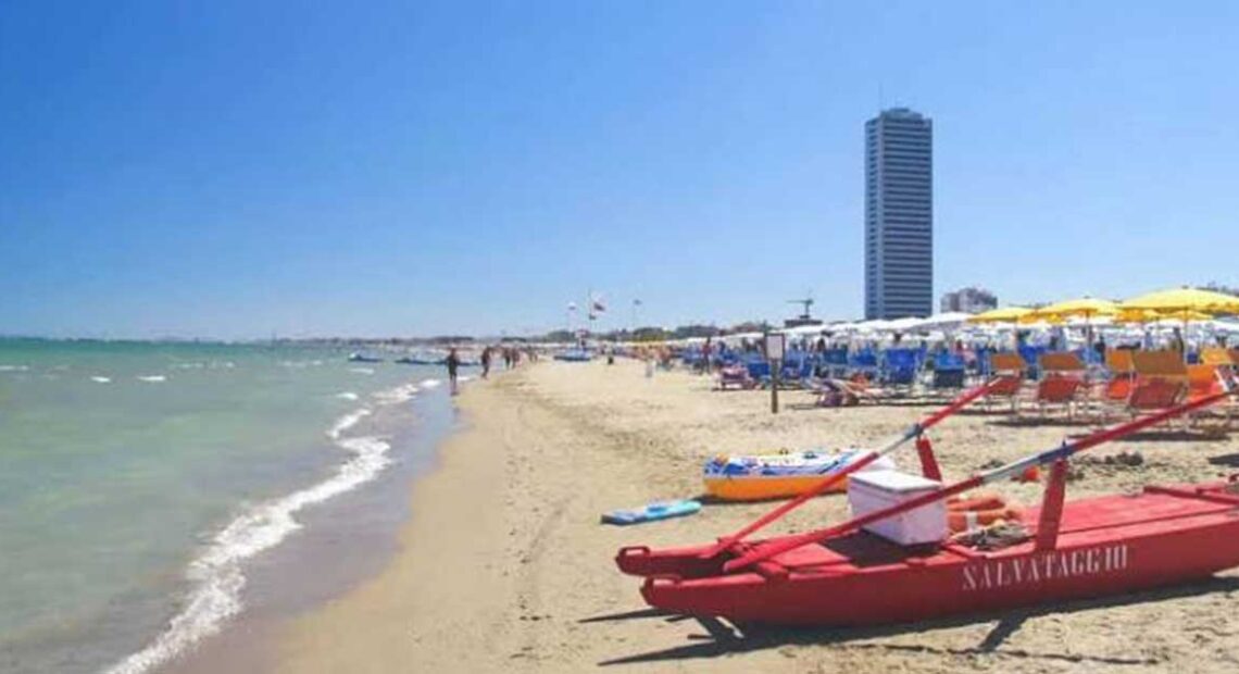 Vista della spiaggia di Cesenatico con pattino di salvataggio rosso in primo piano e il grattacielo sullo sfondo