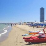 Vista della spiaggia di Cesenatico con pattino di salvataggio rosso in primo piano e il grattacielo sullo sfondo