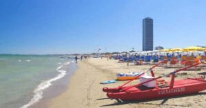 Vista della spiaggia di Cesenatico con pattino di salvataggio rosso in primo piano e il grattacielo sullo sfondo