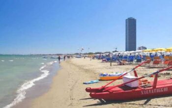 Vista della spiaggia di Cesenatico con pattino di salvataggio rosso in primo piano e il grattacielo sullo sfondo