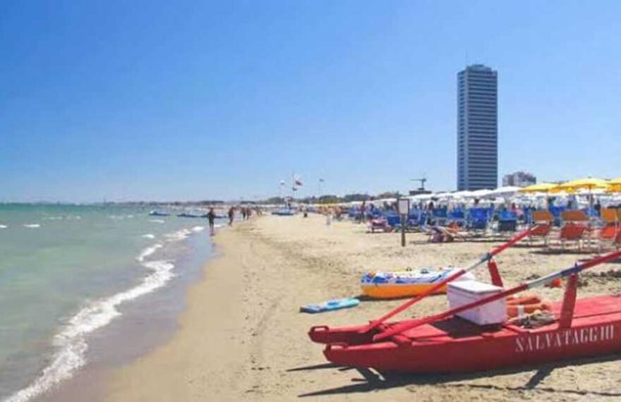 Vista della spiaggia di Cesenatico con pattino di salvataggio rosso in primo piano e il grattacielo sullo sfondo