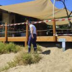 Militare della Guardia Costiera accanto a una veranda in legno sigillata su una duna di sabbia.