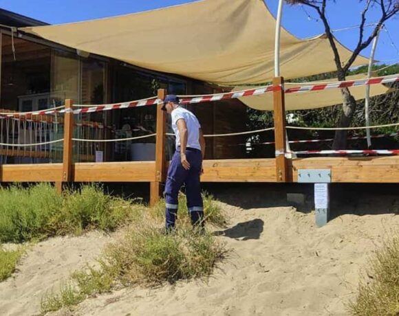 Militare della Guardia Costiera accanto a una veranda in legno sigillata su una duna di sabbia.
