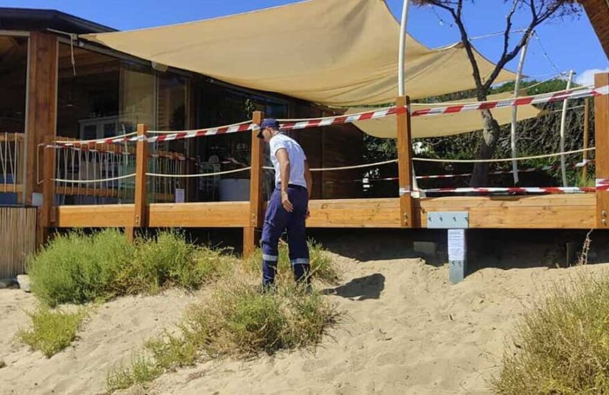 Militare della Guardia Costiera accanto a una veranda in legno sigillata su una duna di sabbia.