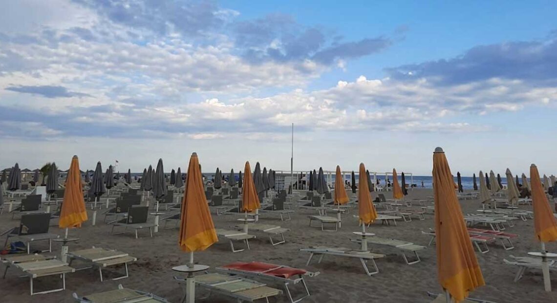 File di ombrelloni arancioni e grigi chiusi con lettini sulla spiaggia di Rimini