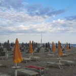 File di ombrelloni arancioni e grigi chiusi con lettini sulla spiaggia di Rimini
