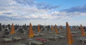 File di ombrelloni arancioni e grigi chiusi con lettini sulla spiaggia di Rimini